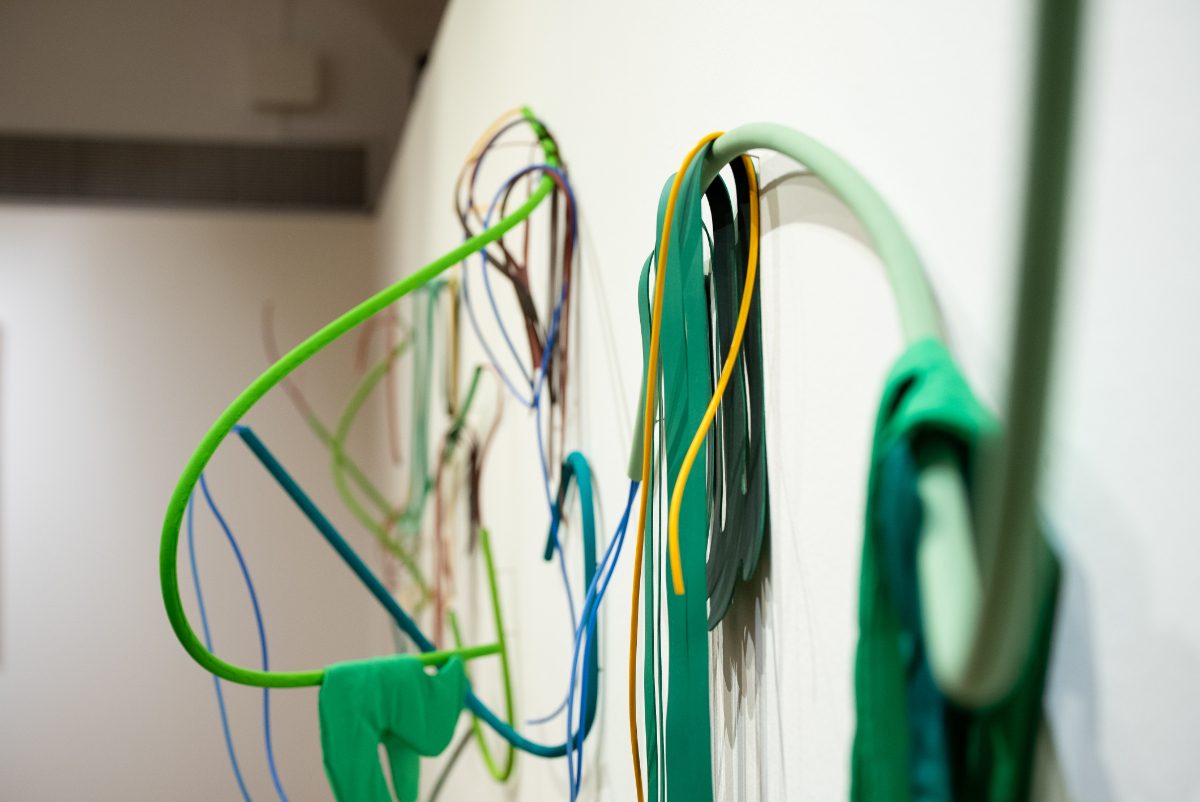 Pormenor de uma escultura de parede: tubos e tiras de plástico em tons de verde, azul e amarelo.